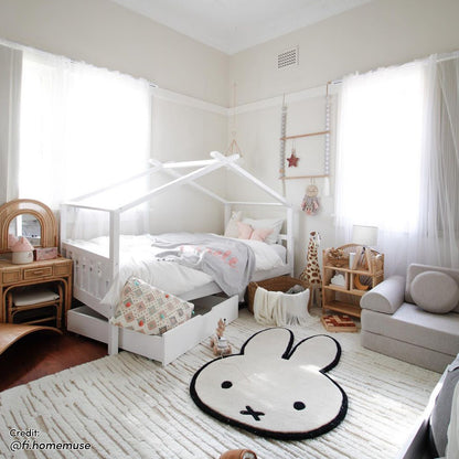 Tucker Solid Pine Timber Kids Bed with Drawers White in a bright children's room, featuring a house-frame design, pastel bedding, and a pull-out drawer underneath. Accompanied by playful decor elements.