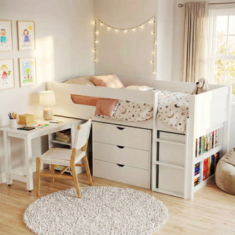 Yuri Solid Pine Storage Loft Bed with Pull Out Desk in White features a raised bed with moon-themed bedding, built-in storage, a desk, and fairy lights, creating a cozy, organized children's corner.