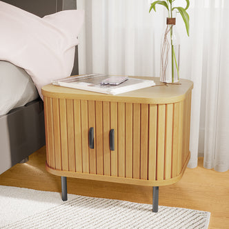 Aaron 50cm Bedside Table with Sliding Doors - Natural, featuring light-toned wood with vertical slats, slim black metal legs, topped with books, a smartphone, and a vase with a plant cutting.