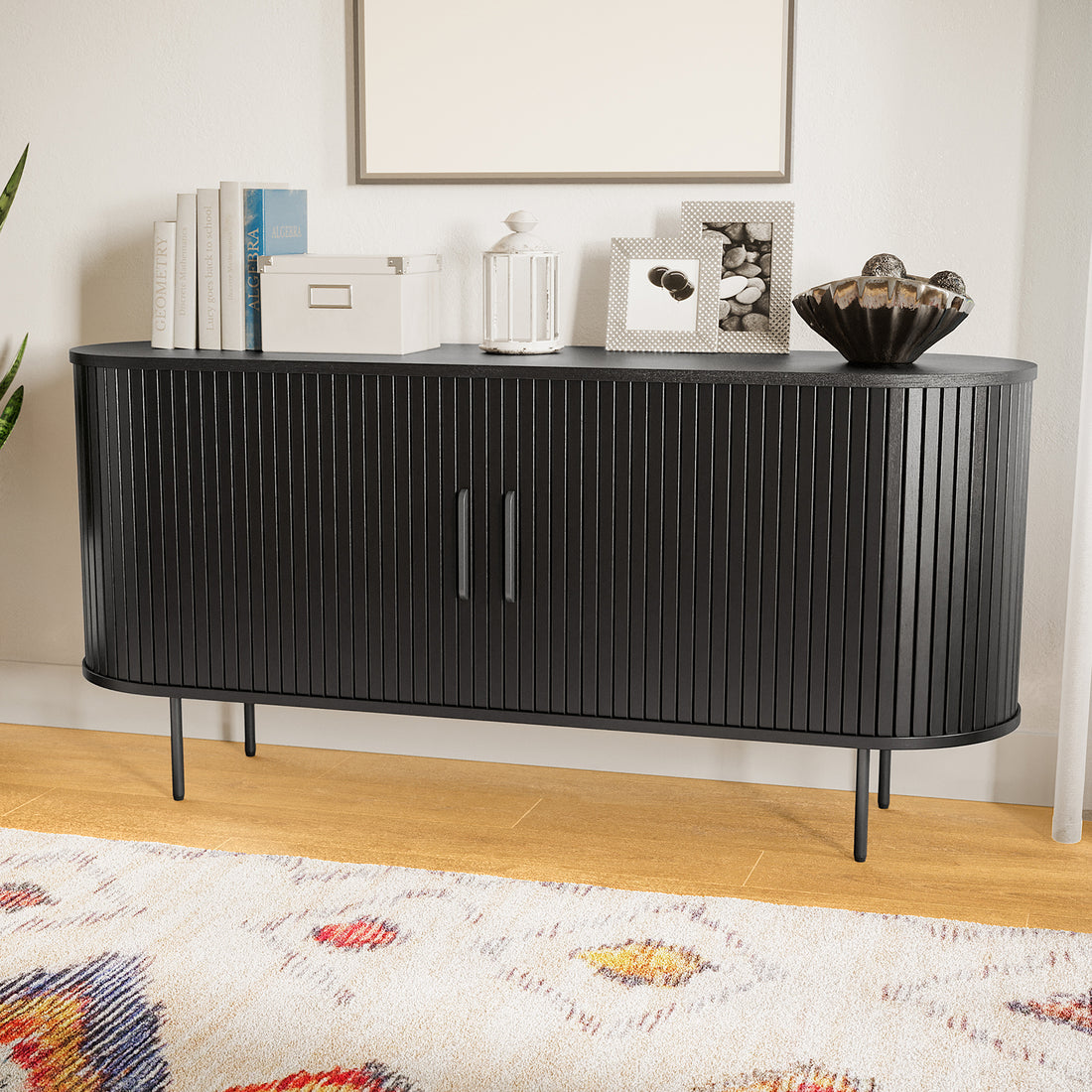 Aaron 140cm Curved Sideboard Buffet - Black features a modern slatted-front design with sleek metal legs, complemented by styled decor, a patterned rug, and a touch of greenery.