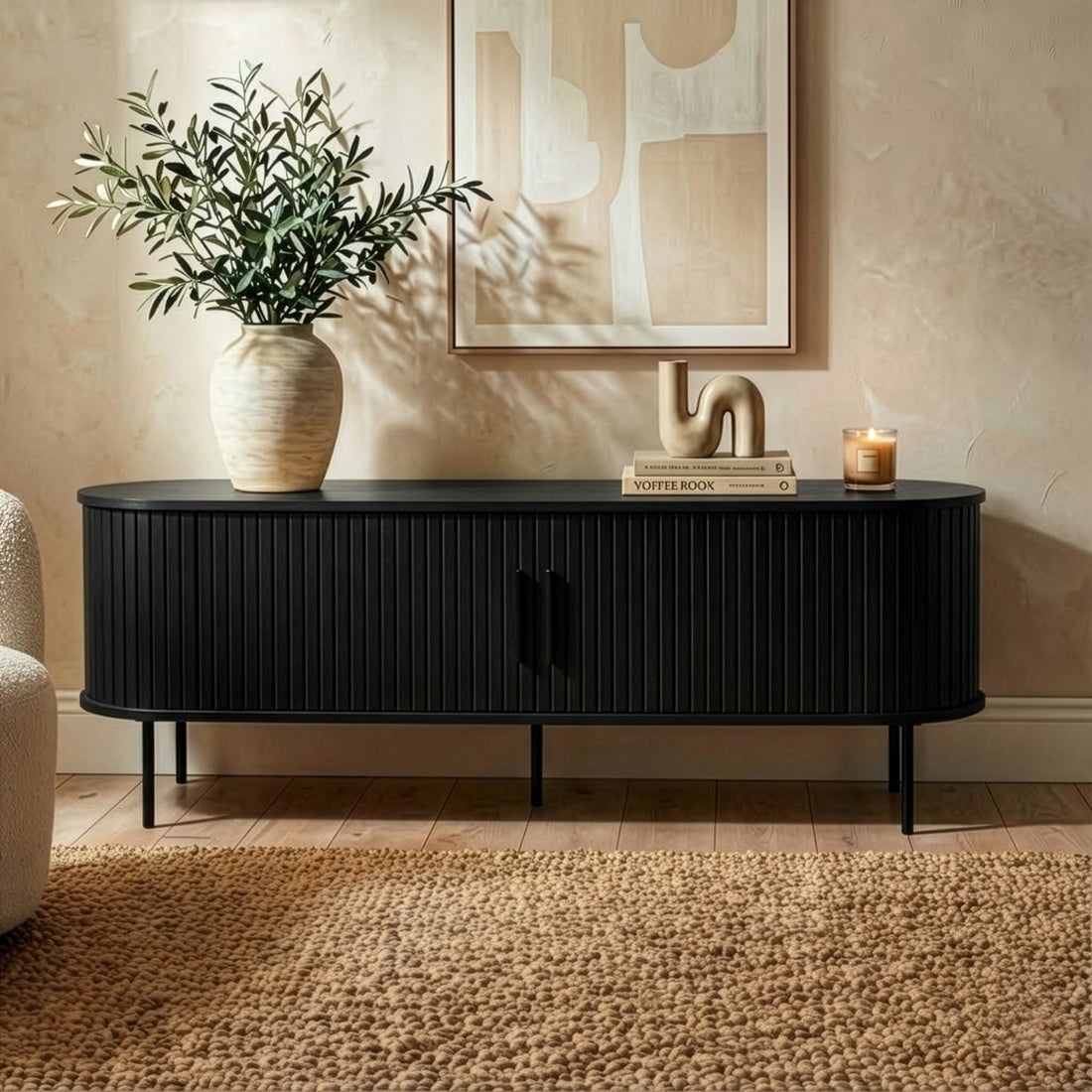 Aaron 160cm Fluted Curved Entertainment TV Unit in Black features a sleek, minimalist design with ribbed detailing and two slatted doors, adorned with decor like a vase, books, and abstract sculpture.