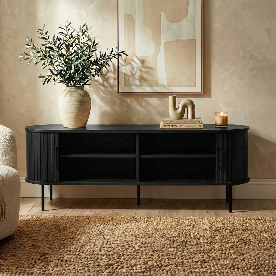 Aaron 160cm Fluted Curved Entertainment TV Unit in Black, featuring slender metal legs and sleek fluted design, adorned with decor including a vase, books, and candle, set against a light wall.