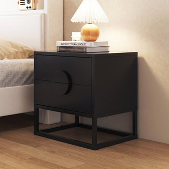 Abigail 55cm 2-Drawer Bedside Table - Black, features a black metal frame, two drawers with arc handles, topped with a lamp, books, and décor, beside a bed with light bedding.