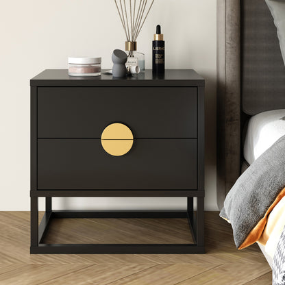 Abigail 55cm 2-Drawer Bedside Table - Black/Gold features a matte black finish with oversized brass knob, set against herringbone floor beside a bed, topped with personal-care items.
