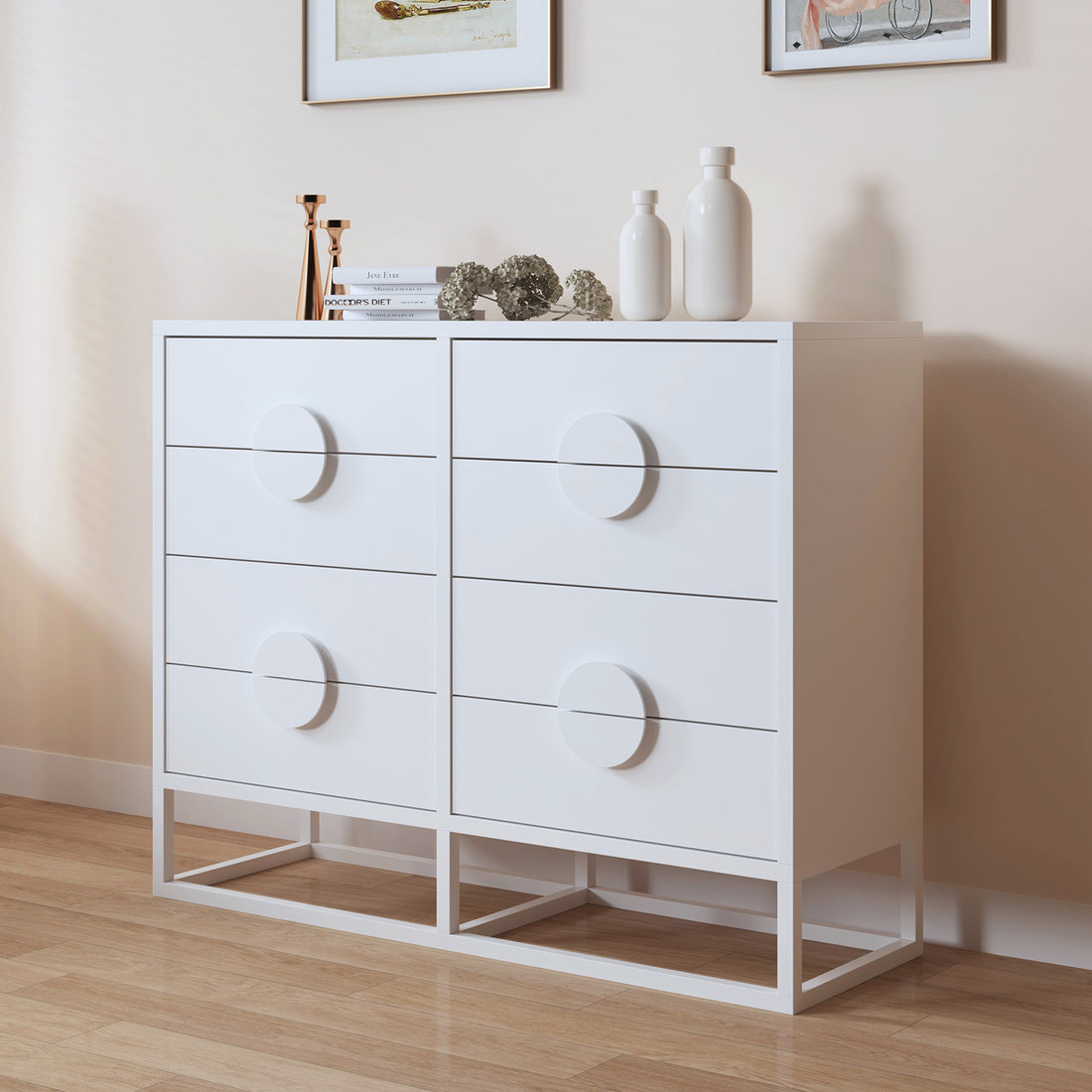 Abigail 120cm Lowboy Dresser with Drawers - White, featuring four drawers with circular pulls, topped with brass candlesticks, books, dried hydrangeas, vases, set against framed art on a beige wall.