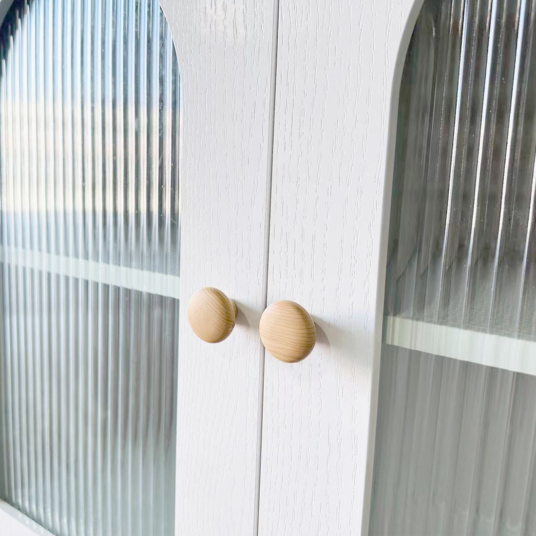Afra 80cm Buffet Cabinet with Glass Doors in White & Natural, showcasing vertically fluted glass panels, round wooden knobs, and a glimpse of the interior shelf through the elegant cabinet doors.