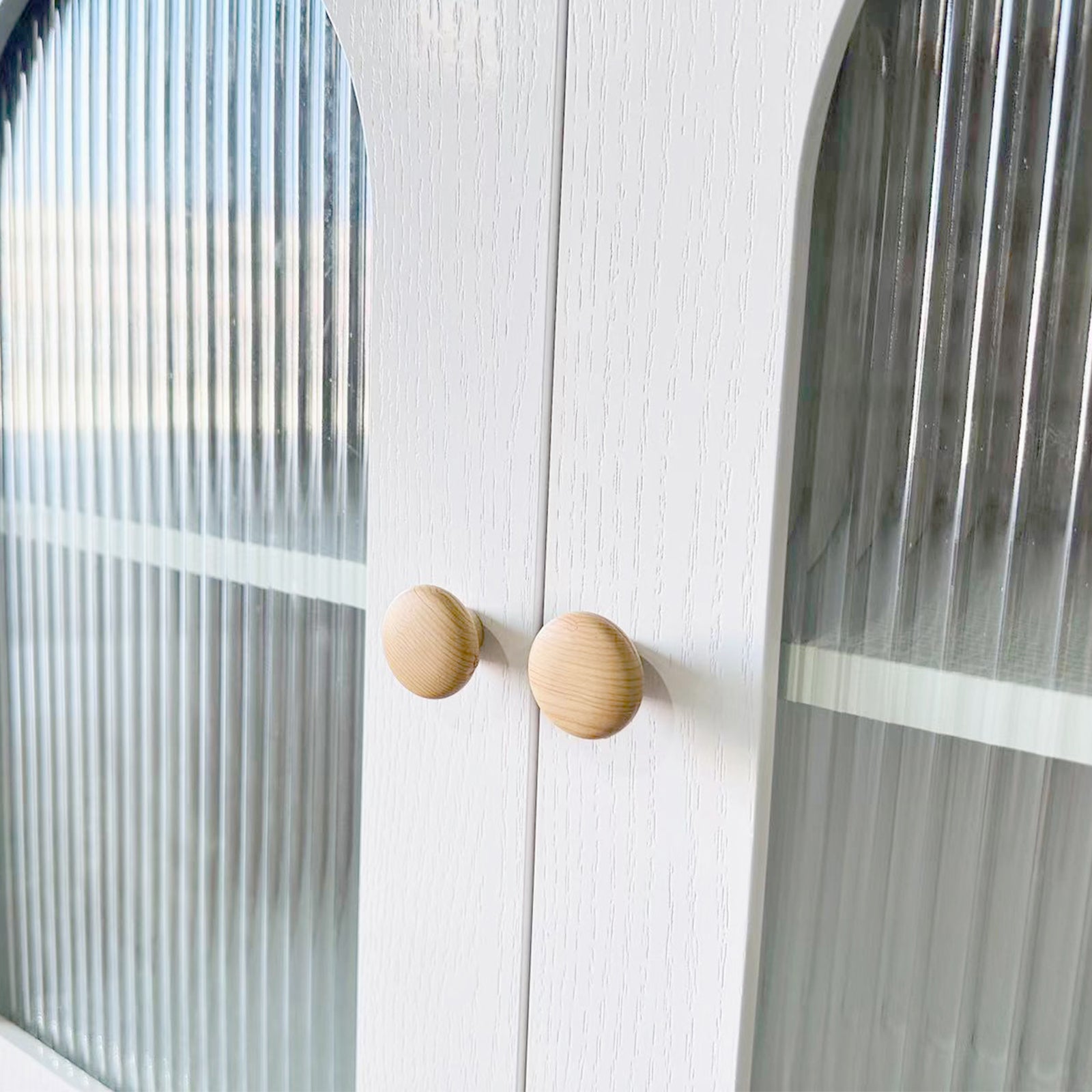 Afra 80cm Buffet Cabinet with Glass Doors in White & Natural, showcasing vertically fluted glass panels, round wooden knobs, and a glimpse of the interior shelf through the elegant cabinet doors.