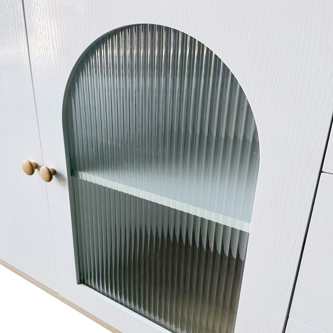 Afra 80cm Buffet Cabinet with Glass Doors features a close-up of its white wooden frame, showcasing an arched, vertically fluted glass panel door and two round wooden knobs on an adjoining solid door.