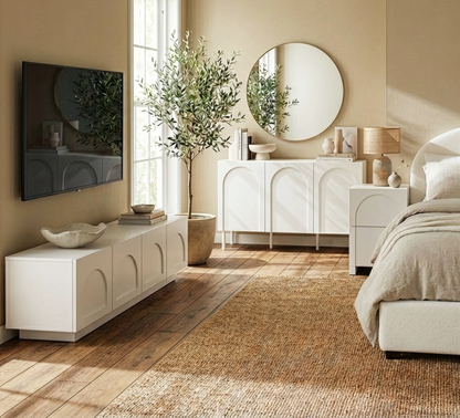 Archen Bedroom & Living Room Storage Package in White showcases a sleek media console, sideboard with round mirror, and bedside table beside a well-dressed bed, all in a minimalist, light-filled room.