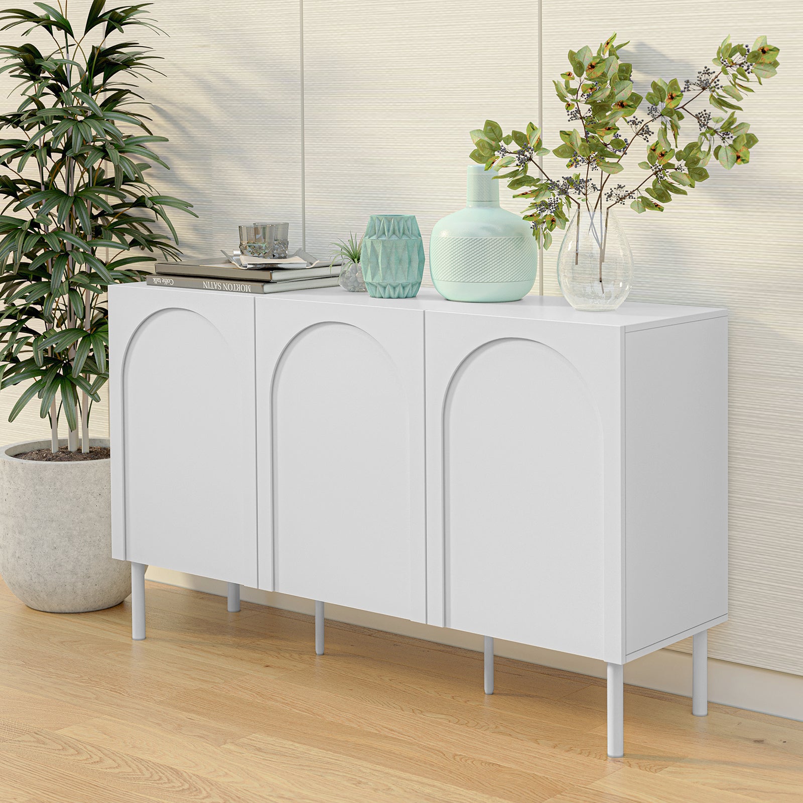 Archen 140cm 3 Door Storage Buffet Sideboard in White, featuring arch-molded doors, slim legs, topped with decor items including vases, books, and a geometric planter, against light wood flooring.