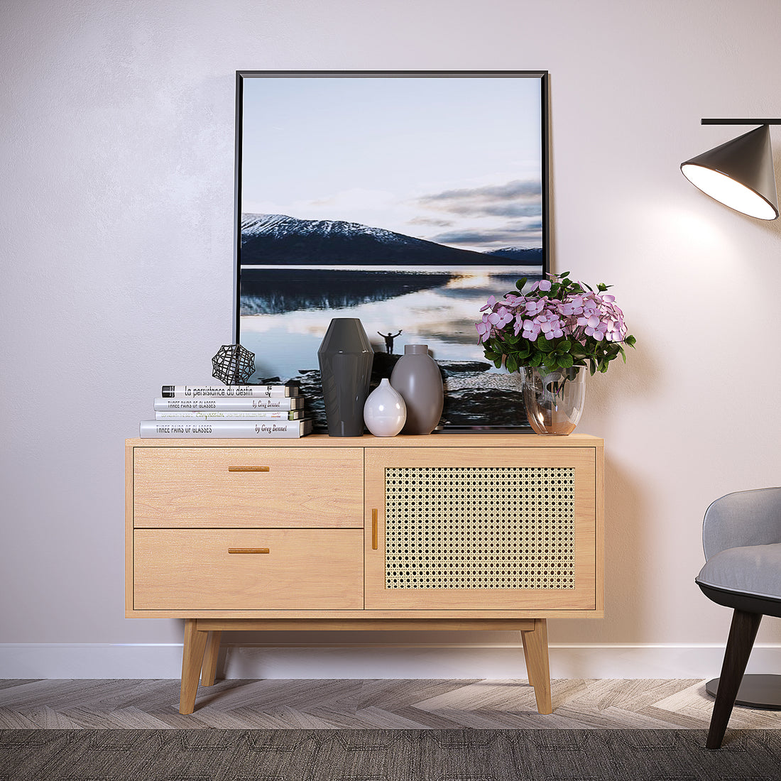 Bethany 120cm Sideboard with Drawers Natural against a pale wall, featuring two drawers and a cane-fronted cabinet, topped with decorative books, vases, and pink hydrangeas, next to a lit floor lamp.