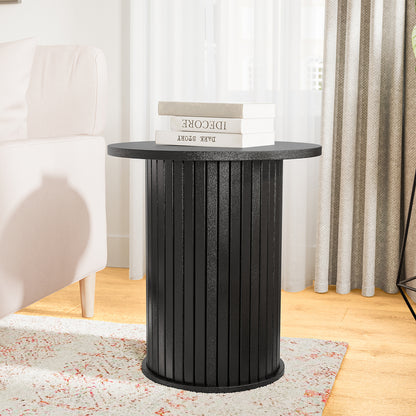 Booker 50cm Round Fluted Oak Side Table in Black, features a drum style with vertical slats, situated on a light rug near a blush sofa, topped with books.