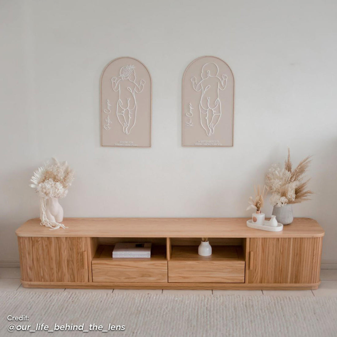 Eddie 200cm Hardwood Oak TV Entertainment Unit in Natural featuring a minimalist design with two central open cubbies, drawers at each end, and decorative dried florals on top.