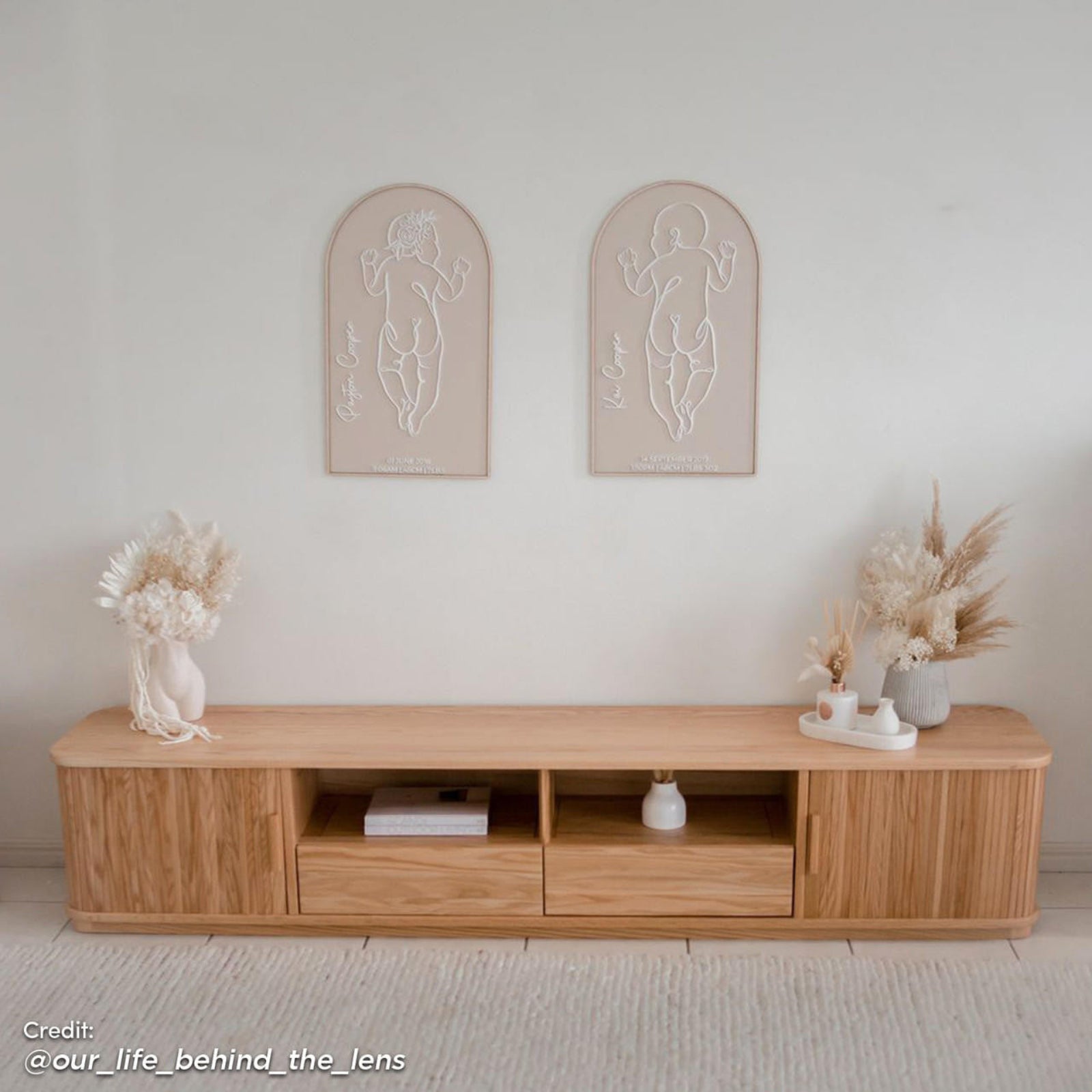 Eddie 200cm Hardwood Oak TV Entertainment Unit in Natural featuring a minimalist design with two central open cubbies, drawers at each end, and decorative dried florals on top.