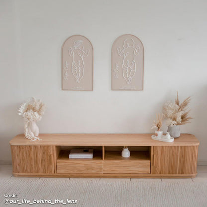 Eddie 200cm Hardwood Oak TV Entertainment Unit in Natural featuring a minimalist design with two central open cubbies, drawers at each end, and decorative dried florals on top.