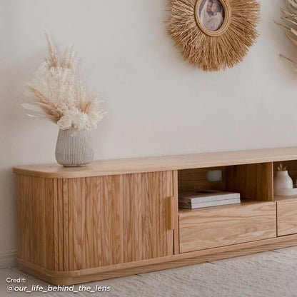 Eddie 200cm American Oak Entertainment Unit in Natural, featuring a minimalist design with open and closed compartments, showcased with a ribbed vase, dried flowers, and coffee-table books on a textured rug.