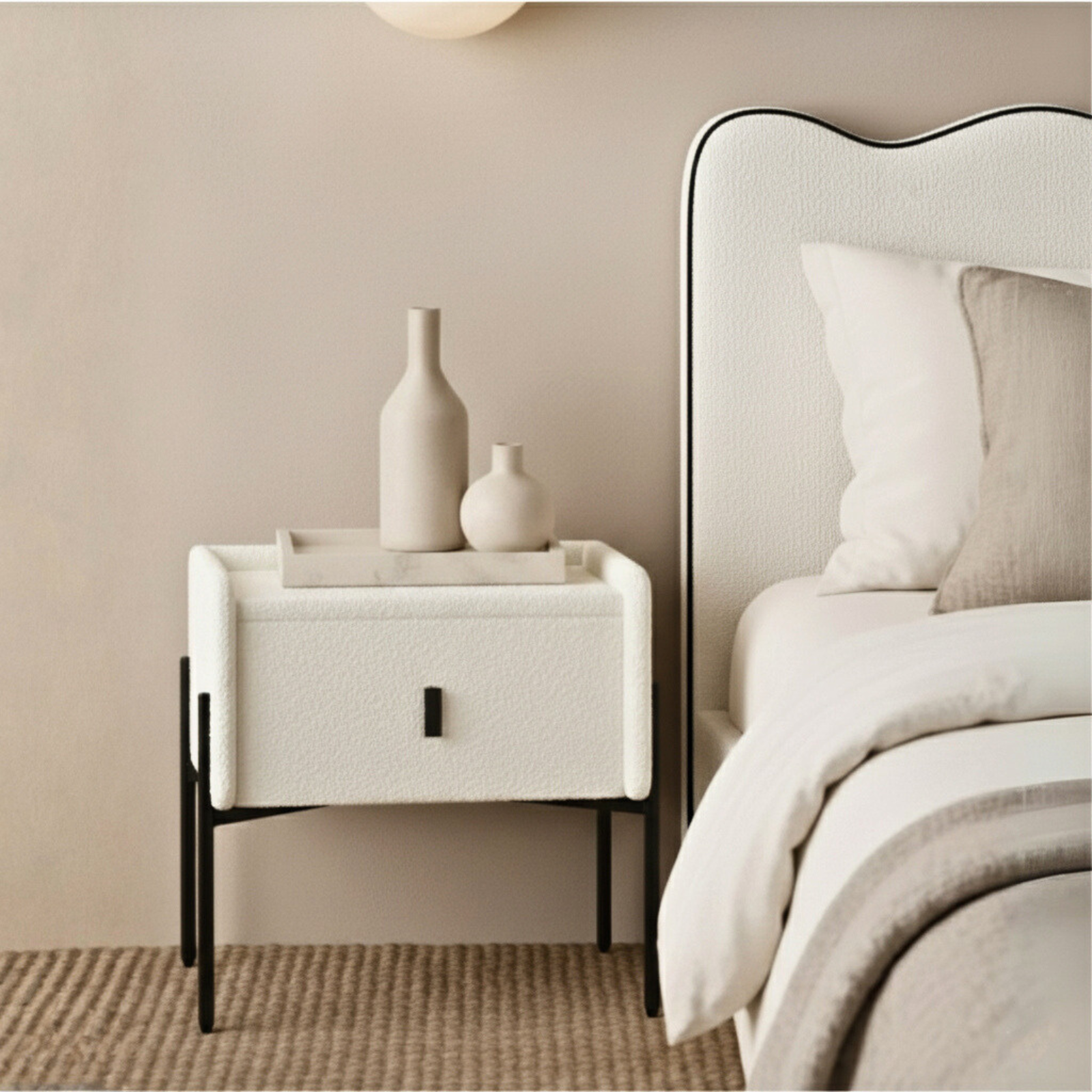 Eliz Boucle Fabric Bedside Table in Cream White, features boucle fabric, slim black metal legs, and a shallow tray with matte ceramic vases, enhancing a modern bedroom corner with a sisal rug.