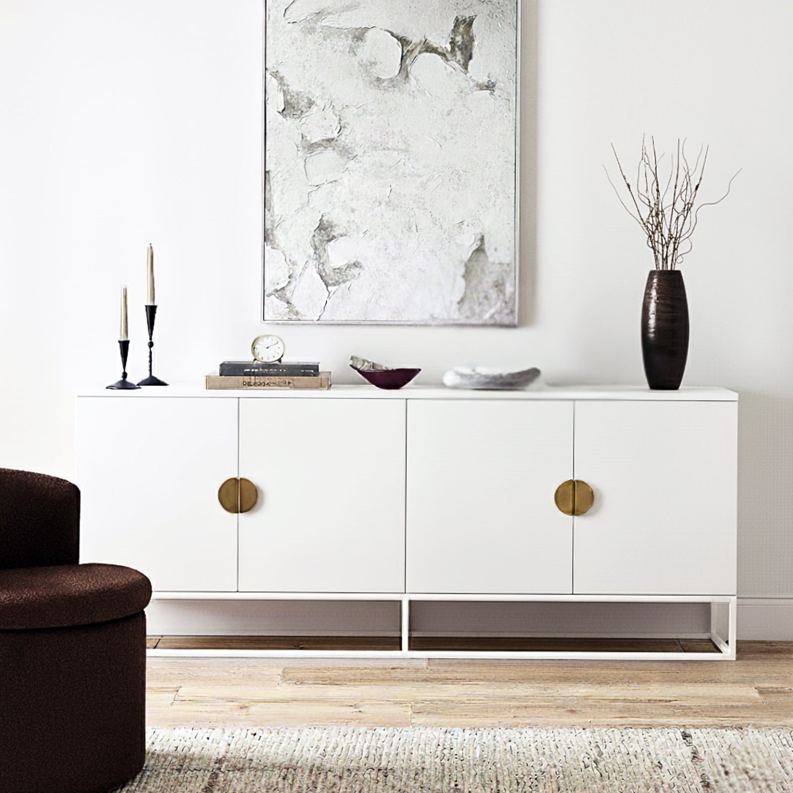 Erick 160cm 4-Door Storage Sideboard Buffet in White is showcased with brass pulls, surrounded by elegant decor including black candleholders, books, a clock, and a vase with twigs.