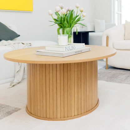 Esmund 90cm Round Coffee Table in Natural with a fluted cylindrical base, topped with art books, a candle, and a vase of tulips, set in a modern living-room setting.