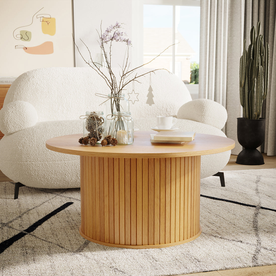 Esmund 90cm Round Coffee Table in Natural features vertical slatted sides, topped with glass jars, pine cones, books, and a ceramic cup, set against a modern living room backdrop.