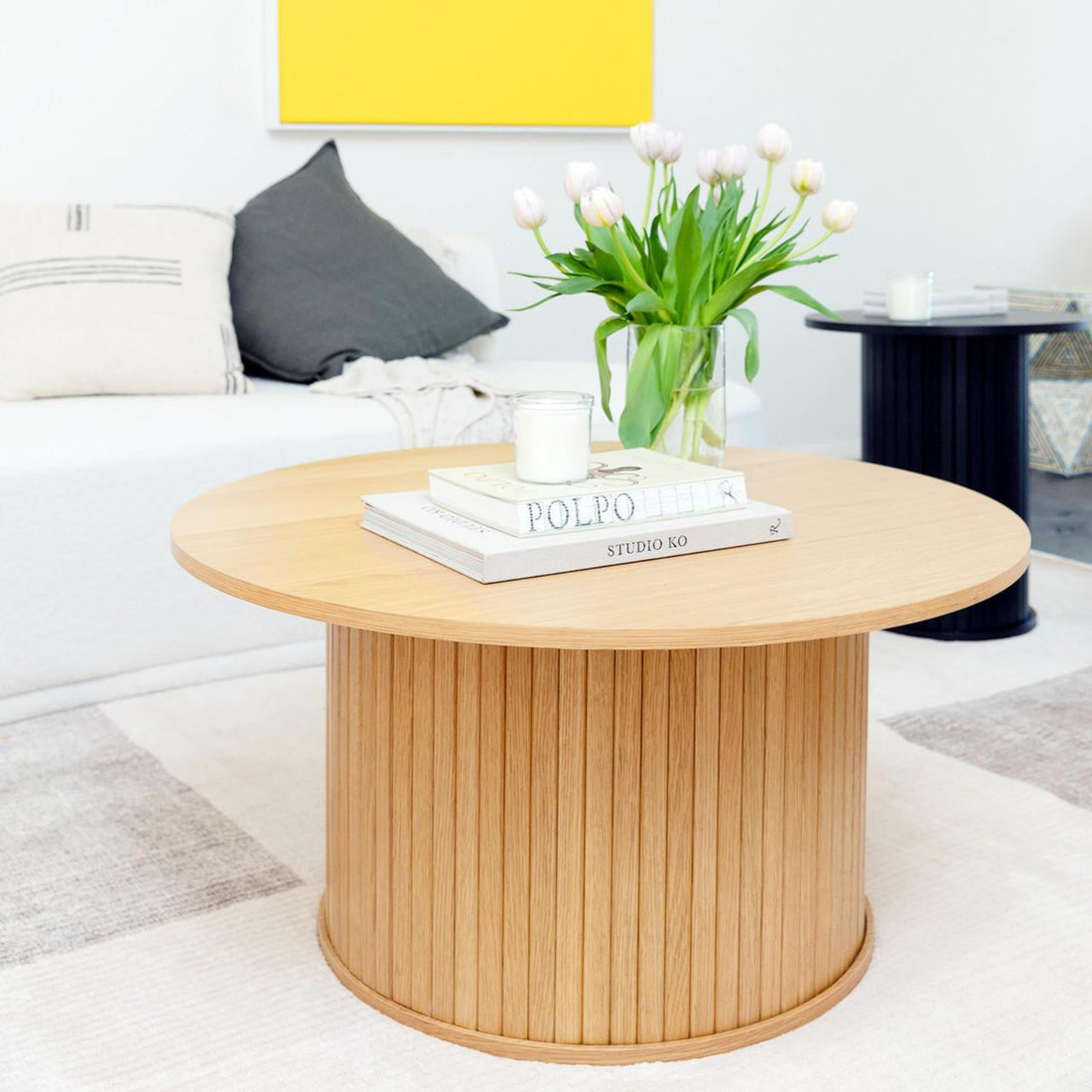 Esmund 90cm Round Coffee Table in Natural, featuring a minimalist design with two books, a candle, and tulips atop. Complements the modern living room's sleek aesthetic seen in the image.