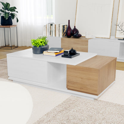 Freda 120cm Coffee Table with Storage in White & Natural, featuring a white and oak-tone surface with a black planter, decorative objects, and books. A modern, organized centerpiece in a bright living room.