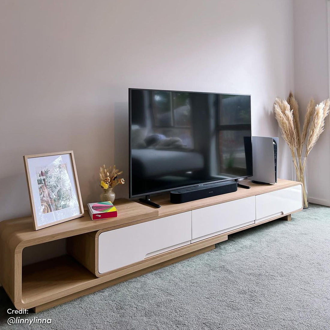Galya Extendable Storage TV Unit - Oak in a minimalist setup with a TV, soundbar, PS5, framed print, books, dried flowers, and pampas grass, showcasing its versatile storage and stylish design.