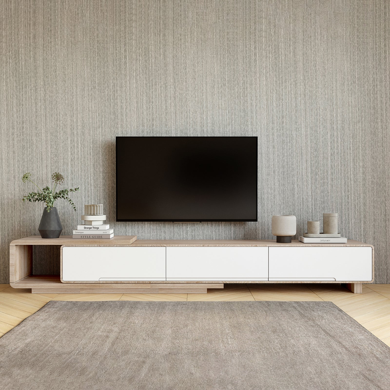 Galya Extendable Storage TV Unit - Oak under a wall-mounted TV, features a light-wood console with white panels, flanked by minimalist decor on a textured wall and herringbone floor.