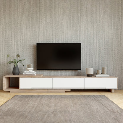Galya Extendable Storage TV Unit - Oak under a wall-mounted TV, features a light-wood console with white panels, flanked by minimalist decor on a textured wall and herringbone floor.