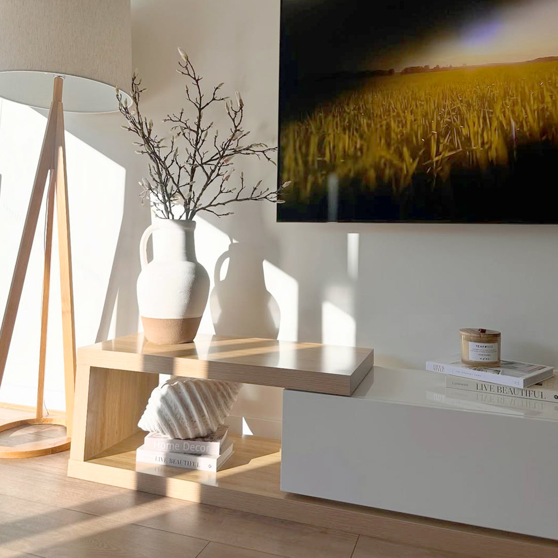 Galya Adjustable Entertainment Storage TV Unit in Oak features a sleek two-tier design with a pale wood finish, topped by a ceramic vase and books, set against a minimalist living-room corner.