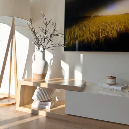 Galya Adjustable Entertainment Storage TV Unit in Oak features a sleek two-tier design with a pale wood finish, topped by a ceramic vase and books, set against a minimalist living-room corner.