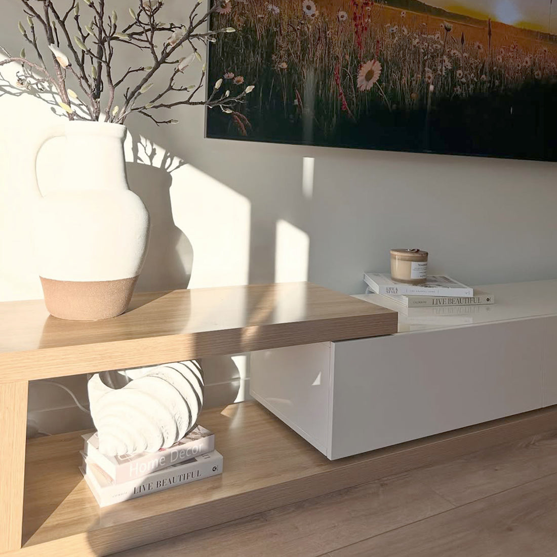 Galya Adjustable Entertainment Storage TV Unit in Oak features a light-wood console with a ceramic vase and TV. The lower shelf displays books and a shell, creating a minimal, stylish look.