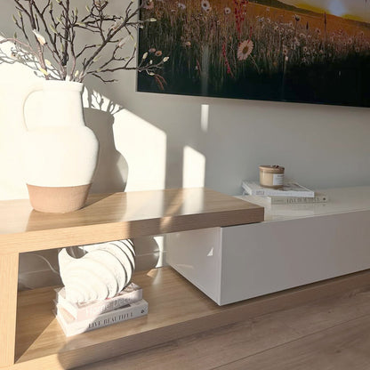 Galya Adjustable Entertainment Storage TV Unit in Oak features a light-wood console with a ceramic vase and TV. The lower shelf displays books and a shell, creating a minimal, stylish look.