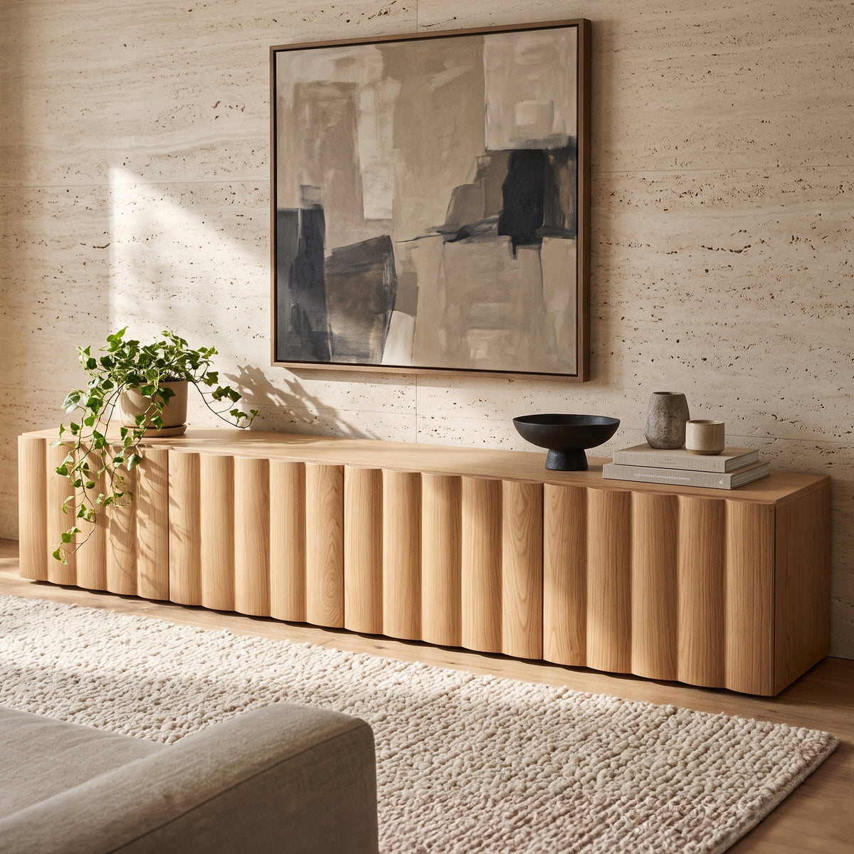 Oak TV unit featuring vertical fluted front panels, styled with a potted trailing plant, decorative ceramic objects, and framed abstract wall art against a textured stone wall.