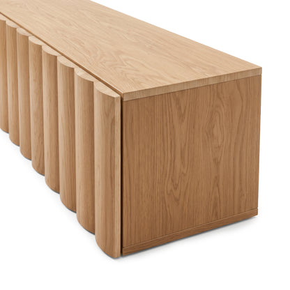 Close-up view of an oak TV unit highlighting the natural wood grain top surface and curved fluted door edges against a plain white studio background.