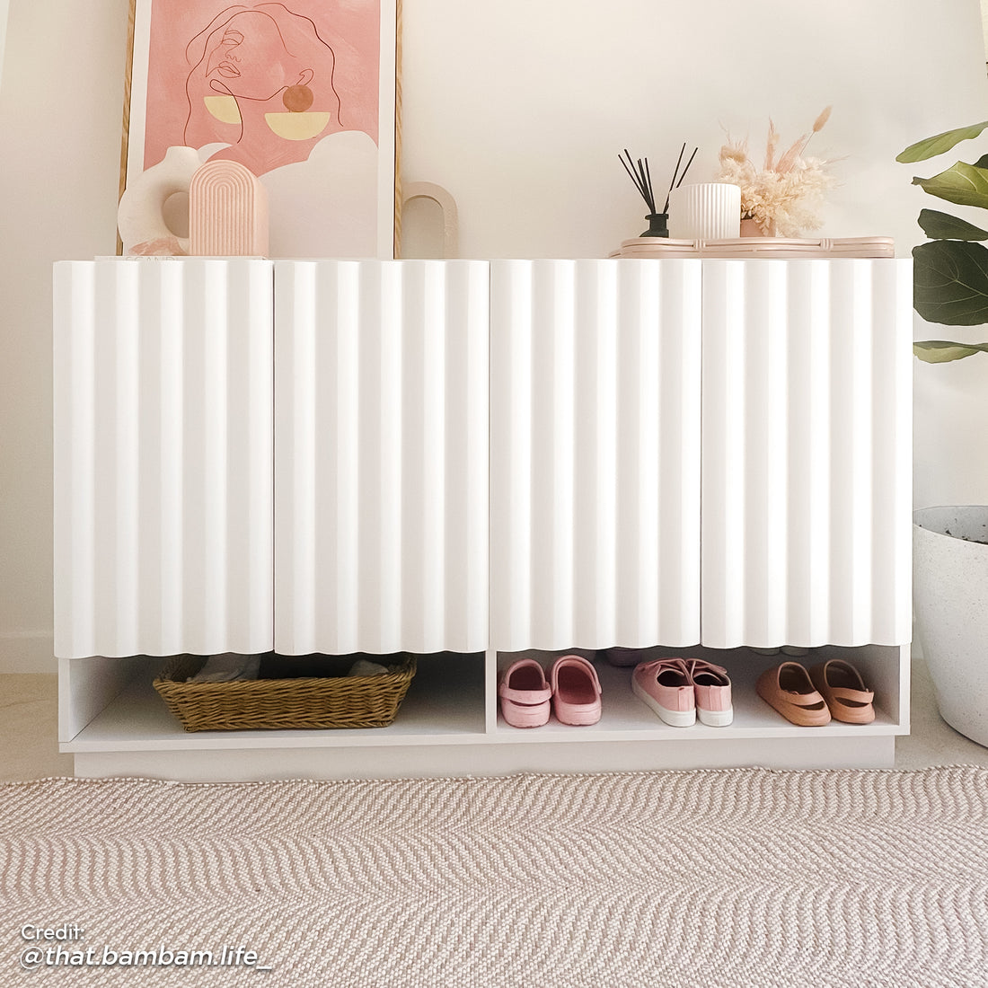 White 4-door fluted shoe cabinet with a bottom open shelf for easy access, styled with pink artwork and home decor in an entryway.