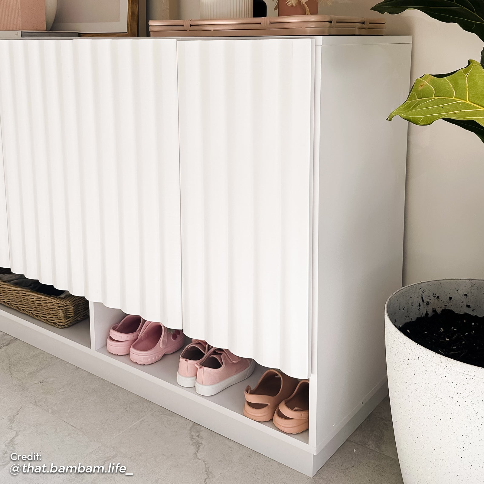 Angled side view of a white fluted shoe storage cabinet with a minimalist vertical slat design and a lower open cubby for organized footwear.