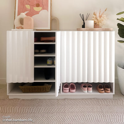 Interior view of a white fluted shoe cabinet with an open door revealing adjustable shelves for hidden storage and an open bottom shelf for sandals and slippers.
