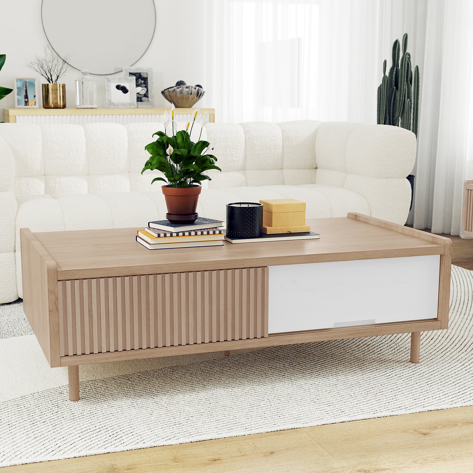 The Hayden 130cm Fluted Coffee Table with Storage in Natural features a light-wood frame, slatted and smooth white panels, topped with a terracotta peace lily, books, a candle, and mustard boxes.