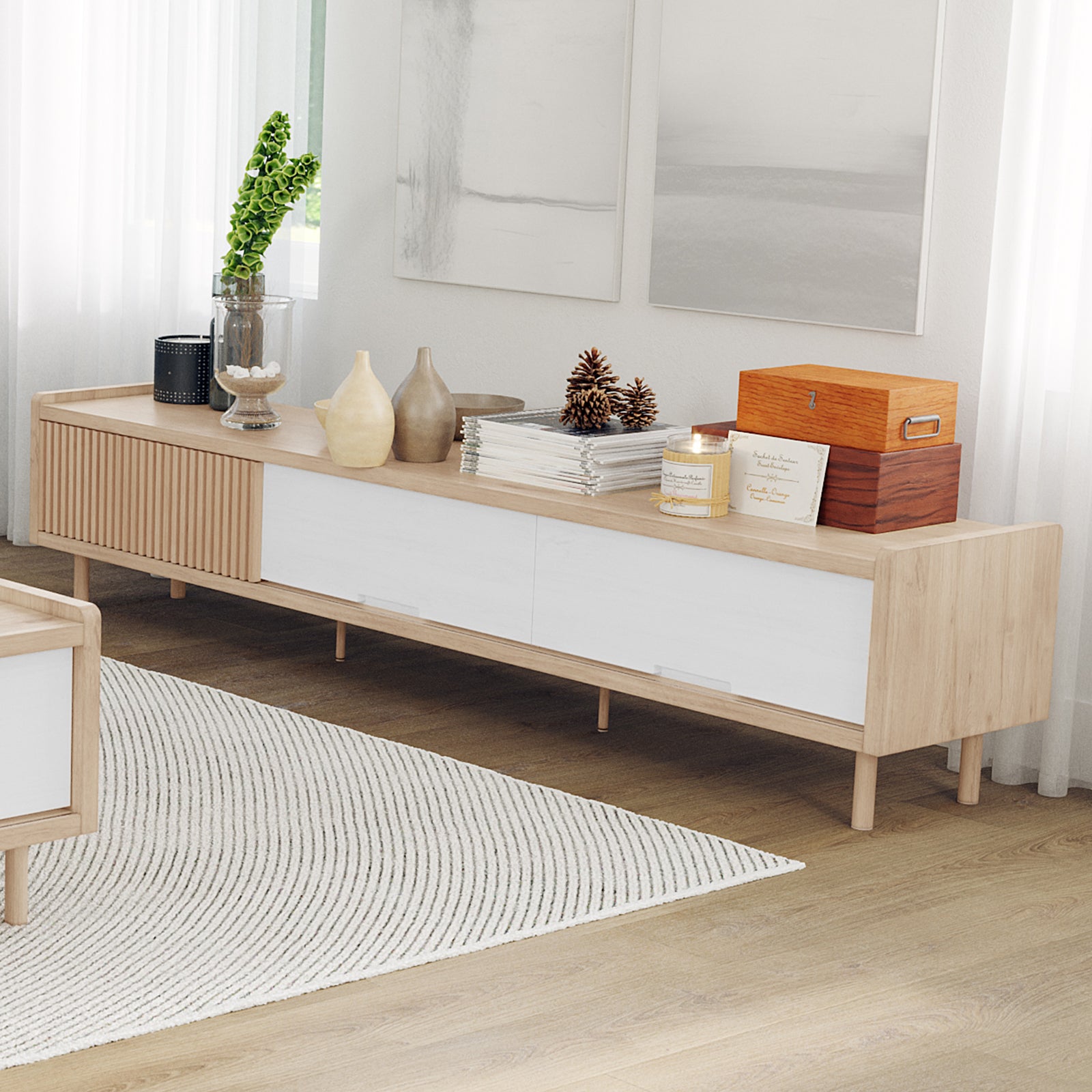 Hayden 200cm Fluted TV Entertainment Unit in Natural features a sleek design with white sliding doors, topped with decor including vases, magazines, and a lit candle, enhancing a modern living room.