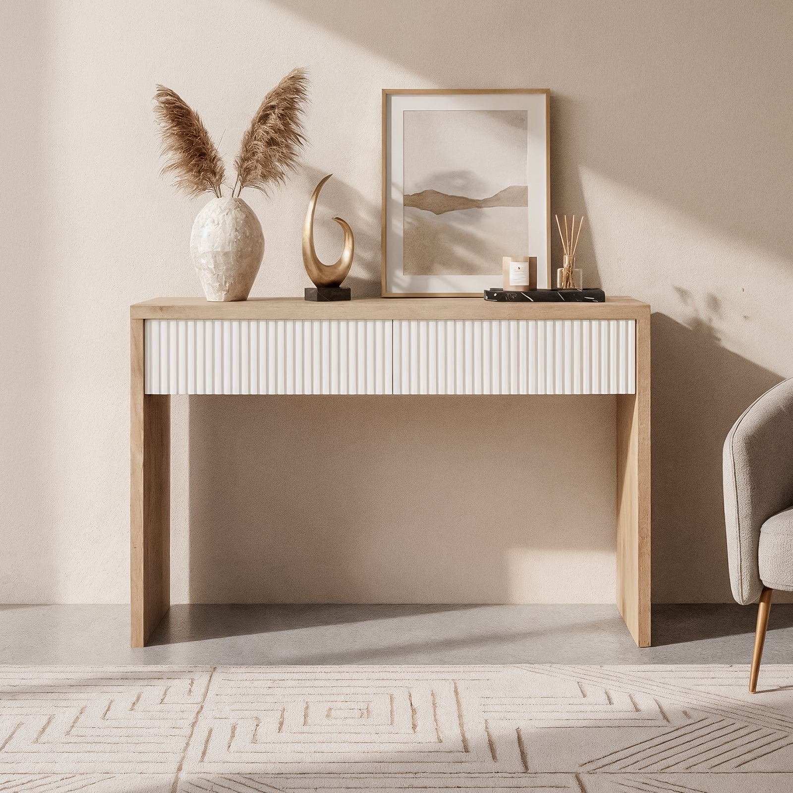 Hayden 120cm Fluted Hallway Table with Storage in Natural, featuring a white fluted-front drawer, pampas grass vase, abstract sculpture, tray with candle and diffusers; paired with a gray chair.