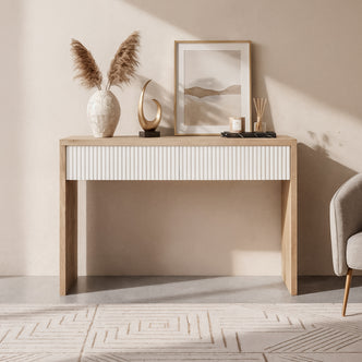 Hayden 120cm Fluted Hallway Table with Storage in Natural, featuring a white fluted-front drawer, pampas grass vase, abstract sculpture, tray with candle and diffusers; paired with a gray chair.