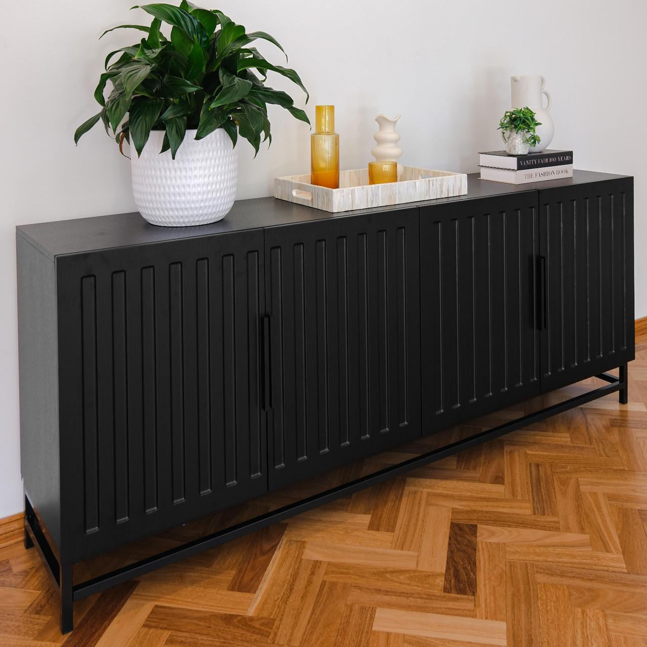 Holly 180cm Sideboard Buffet Table with Steel Legs in Black against a light wall, adorned with a white planter, wood tray with amber vases, and stacked books with decorative accents on top.