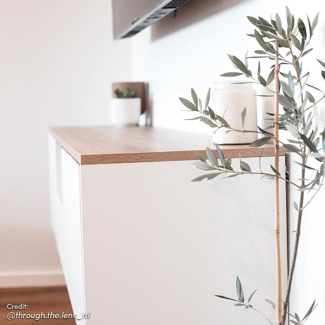 Leslie 180cm Floating Entertainment Unit in White & Natural, featuring a sleek white cabinet with a light wood top, a small succulent, jar candle, and twig branch, under a wall-mounted screen.