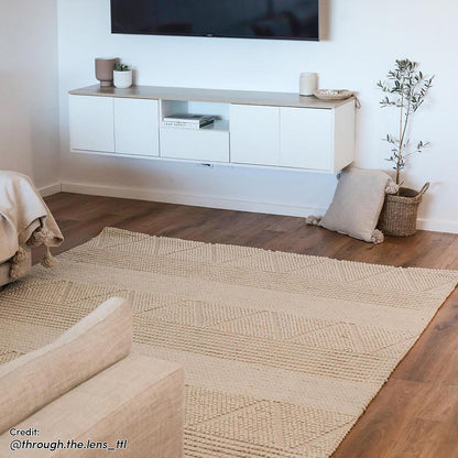 Leslie 180cm Floating Entertainment Unit in White & Natural, wall-mounted with a light wood top, holds decor and a TV above, enhancing the softly-lit, neutral living space.