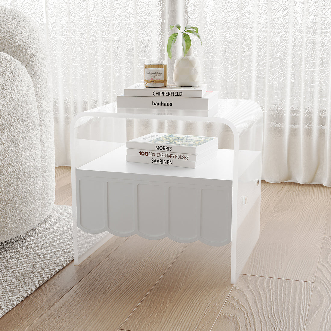 Magdalena 45cm Scalloped Acrylic Bedside Table in White with clear acrylic sides, a scalloped-front lower shelf, topped with a vase, candle, and stacked art books, next to a boucle sofa.