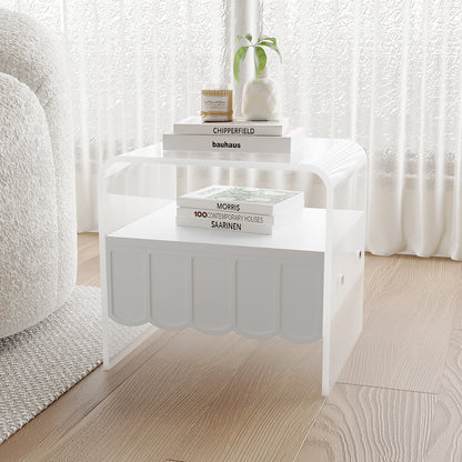 Magdalena 45cm Scalloped Acrylic Bedside Table in White with clear acrylic sides, a scalloped-front lower shelf, topped with a vase, candle, and stacked art books, next to a boucle sofa.