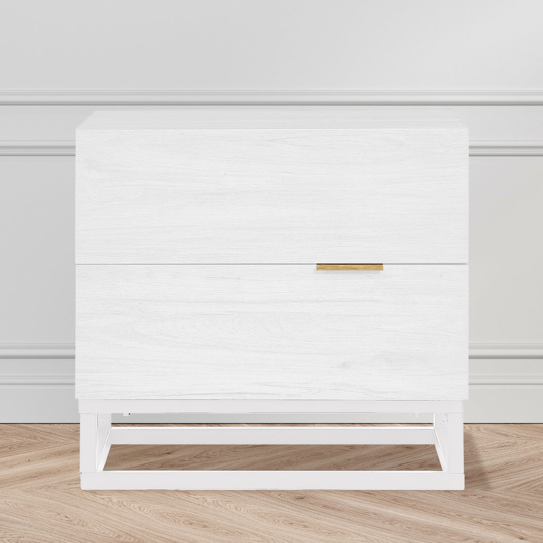 Manuel 2 Drawer Storage Bedside Table White with white wood grain finish, two drawers, slim brass-tone handle, and a simple white metal frame, against a light-grey wall on oak-tone floor.