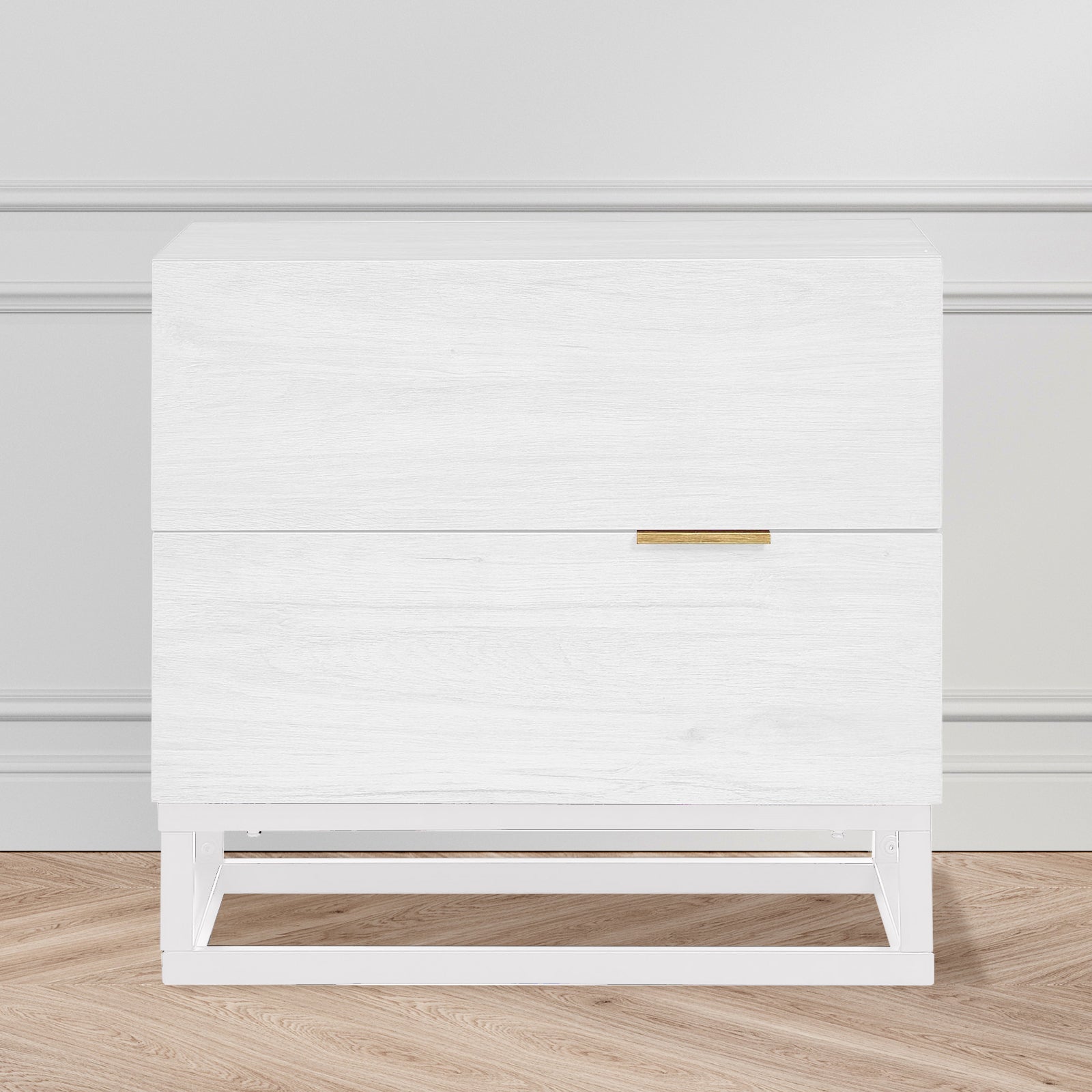 Manuel 2 Drawer Storage Bedside Table White with white wood grain finish, two drawers, slim brass-tone handle, and a simple white metal frame, against a light-grey wall on oak-tone floor.
