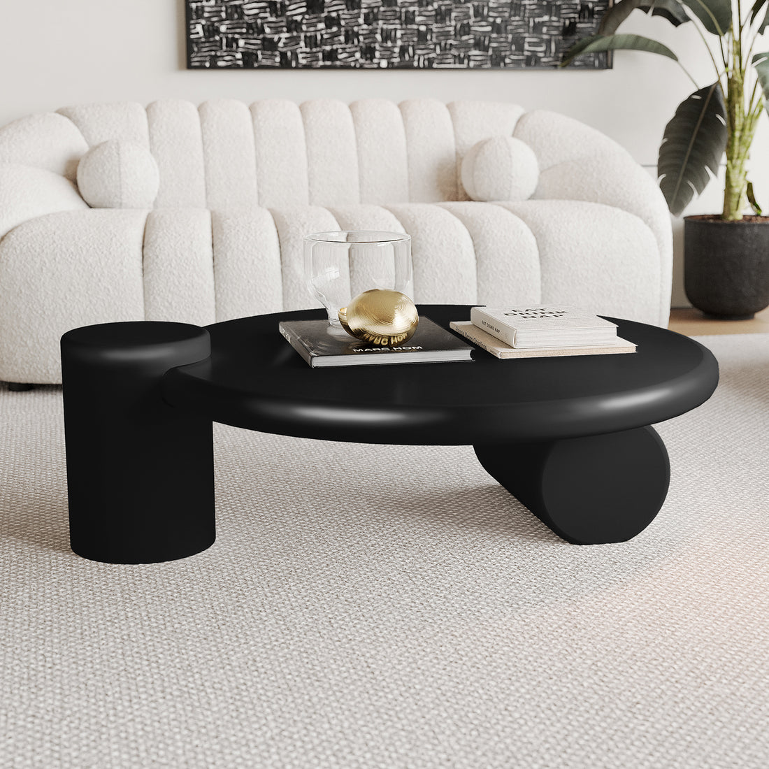 Nando 100cm Modern Round Coffee Table in Black featuring dual cylindrical supports, a glass tumbler, gold decorative orb, and books. Complements an off-white sofa and abstract artwork in a minimalist setting.